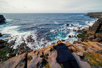 High angle view of a woman lying on a cliff overlooking the ocean