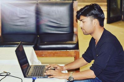 Side view of young man using laptop at table