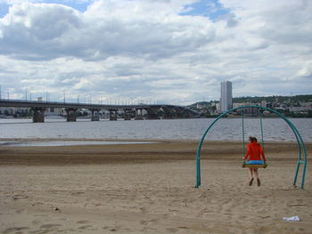 Rear view of woman standing on beach against sky