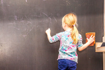 Rear view of girl writing on blackboard