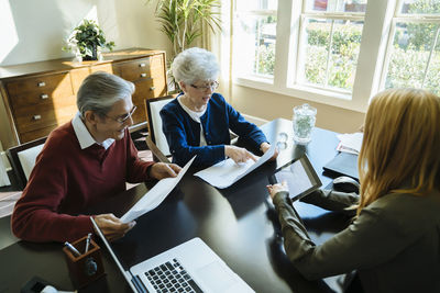 High angle view of senior couple reading documents while discussing with financial advisor in office