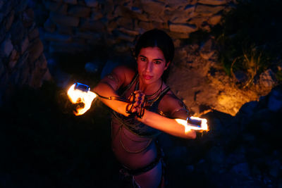 From above talented female fire dancer in costume standing with burning fire fans during performance in medieval village