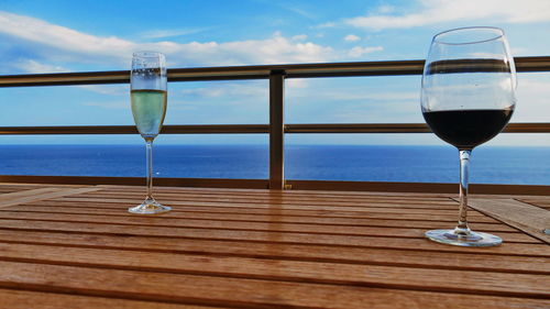 Wine glass on table by sea against sky