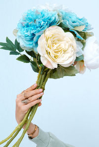 Close-up of hand holding flowers against white background