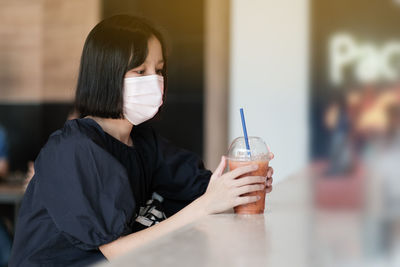 Woman wearing mask while holding drink on table at cafe