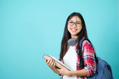 Portrait of smiling young woman using smart phone against blue background