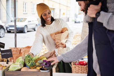 Smiling woman buying fresh vegetables from male market vendor at fruit stall