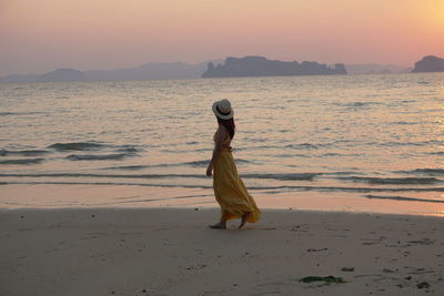 Woman walking on beach against sky during sunset