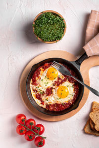 Flat lay image of shakshouka in a pan on a light coloured background close up