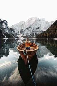 Rear view of woman sitting in moored boat at lake against sky