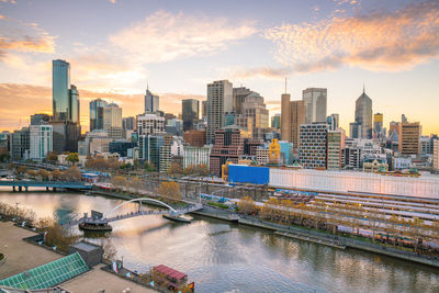 Bridge over river by buildings against sky during sunset