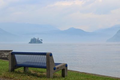 Empty bench by lake against sky