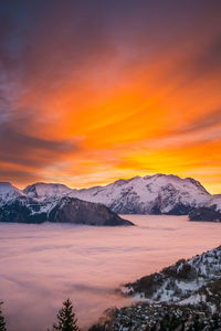 Scenic view of lake by snowcapped mountains against orange sky