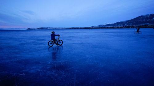 Man riding bicycle in water against blue sky