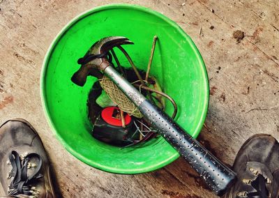 High angle view of hammer in green container by shoes on table