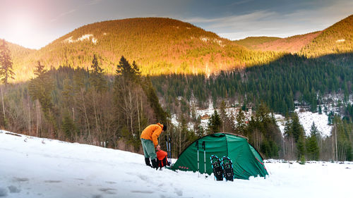 Man standing by tent against trees during winter