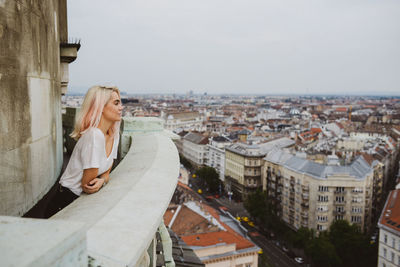 Blonde girl looking over the city from a balcony in daylight