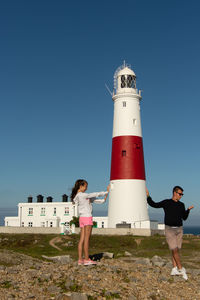 Full length of man and a woman standing by lighthouse against clear blue sky