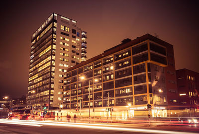 Light trails on road by buildings against sky in city at night