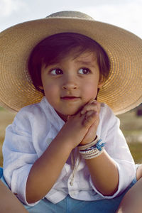 Baby boy in straw hat and blue pants sitting on a haystack in a field in autumn