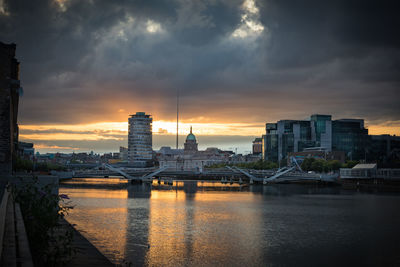 Bridge over river against buildings in city during sunset