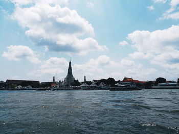 Buildings by sea against cloudy sky