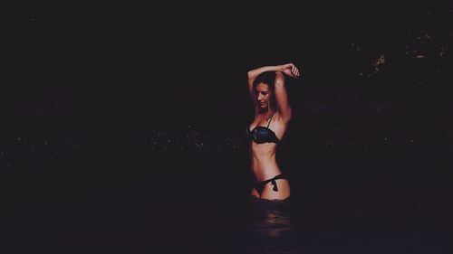 Young woman in bikini standing against black background