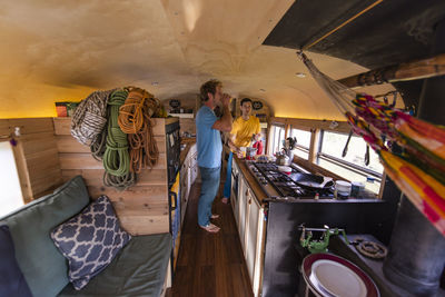 Two people drinking beverage inside converted school bus with ropes