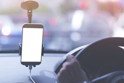 Cropped hand on steering wheel with smart phone in car