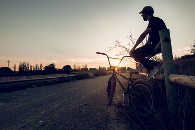 Man riding bicycle on road against sky at sunset