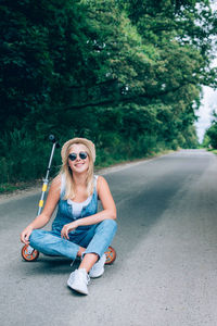 Portrait of young woman sitting on road against trees