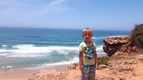 Portrait of boy standing at beach against sky