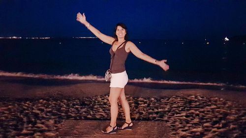 Woman with arms raised on beach against sky at night