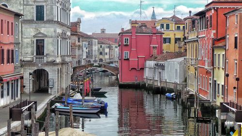 Boats moored in canal amidst buildings against sky