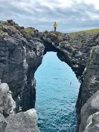 Man standing on natural arch over sea against sky