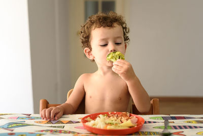 Cute girl holding food while sitting by table at home