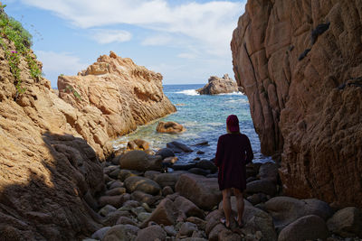 Rear view of woman standing on rocks at sea 