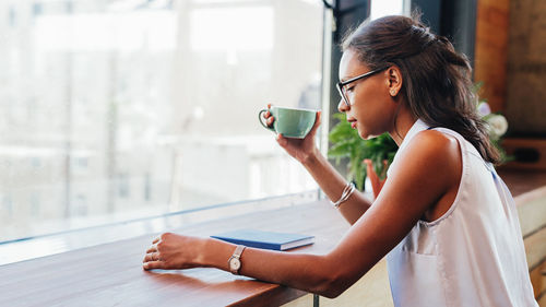 Woman drinking coffee while reading book at table