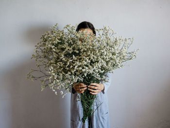 Woman holding plants against wall