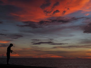 Silhouette man fishing on beach against sky during sunset