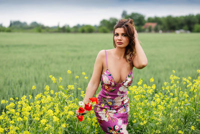 Portrait of beautiful young woman standing amidst flowers on land