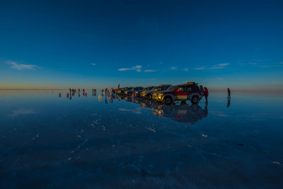 Silhouette people with off-road vehicles at beach against blue sky during sunset