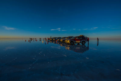 Silhouette people with off-road vehicles at beach against blue sky during sunset