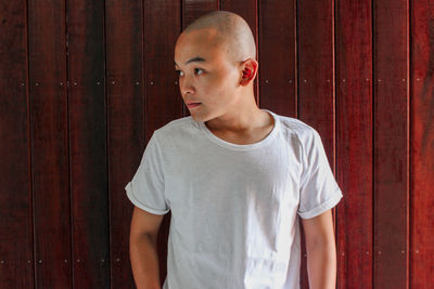 Portrait of young man standing against wooden wall