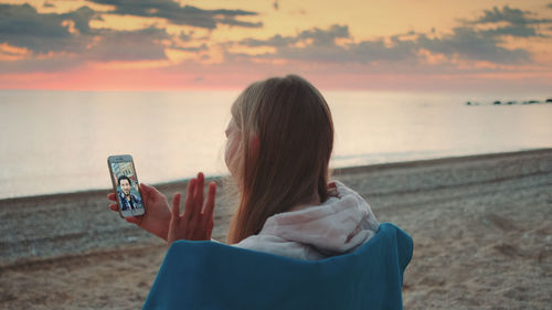 Rear view of man using mobile phone at beach during sunset