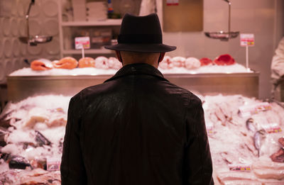 Rear view of adult man in hat in front of fish store in market. madrid, spain