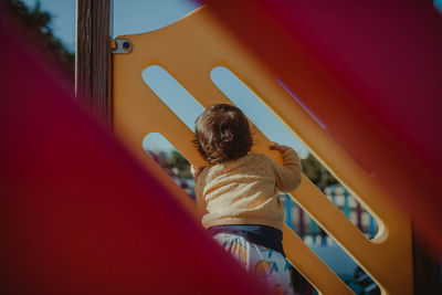 Rear view of baby girl standing on outdoor play equipment in playground