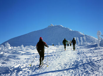 Rear view of people on snowcapped mountain against clear blue sky