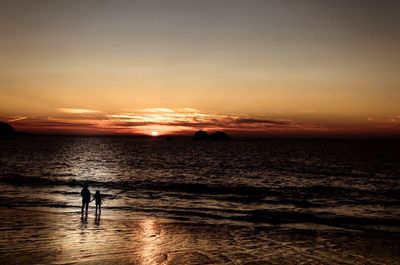 Silhouette people on beach against sky during sunset