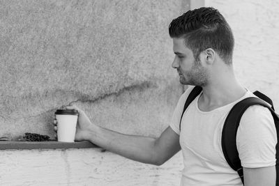 Young of man holding coffee cup against wall